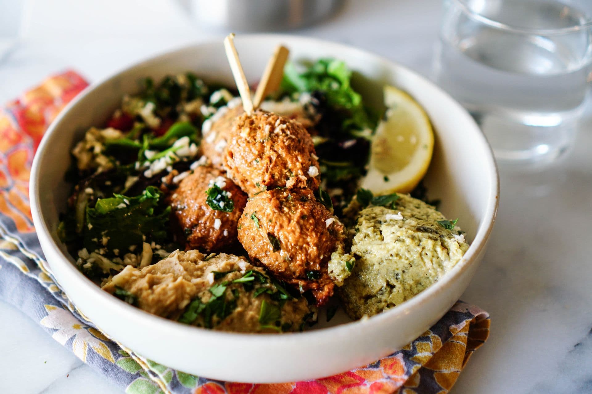 Falafel on skewers over greens and hummus in a bowl