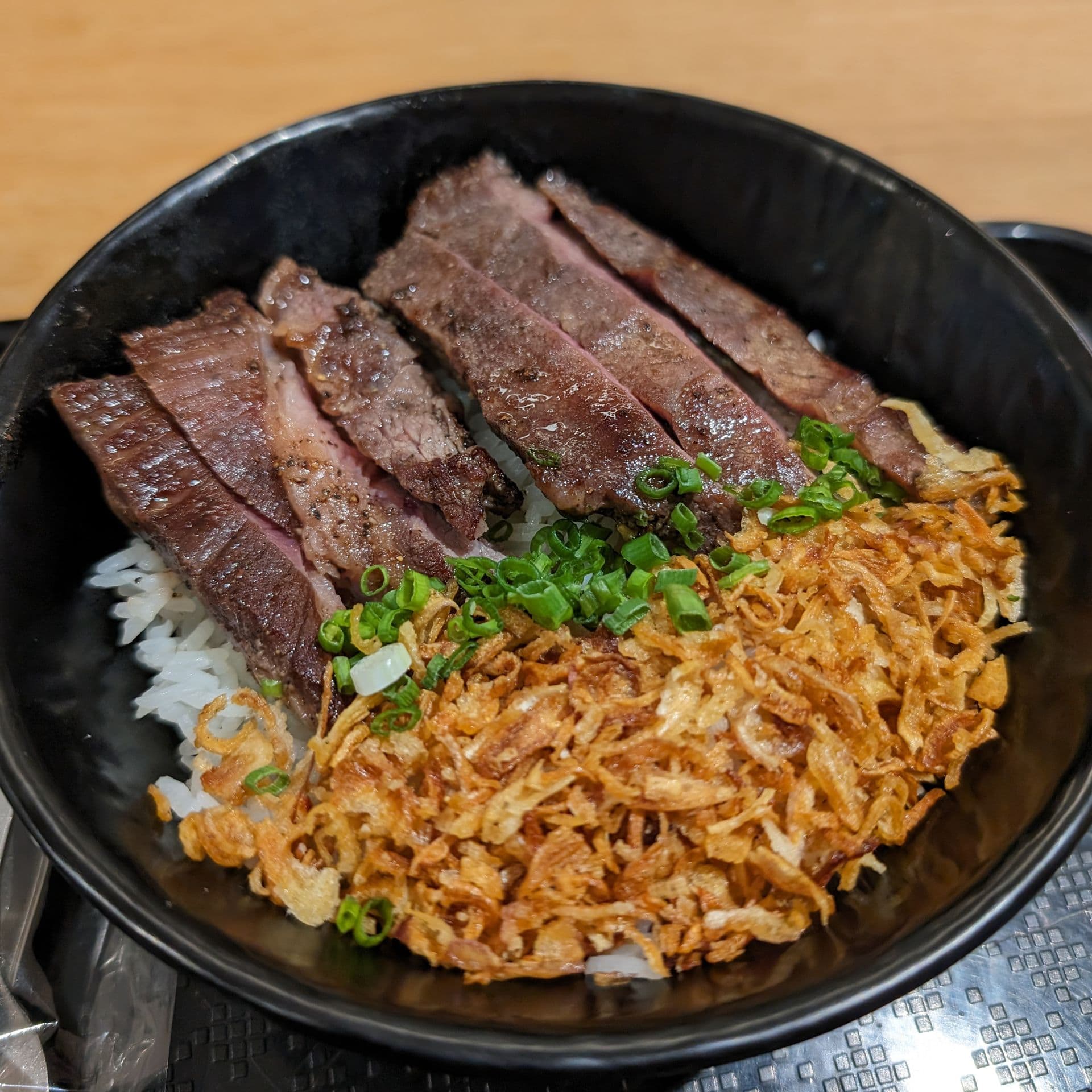 Sliced seared steak over rice with scallions and crispy onions
